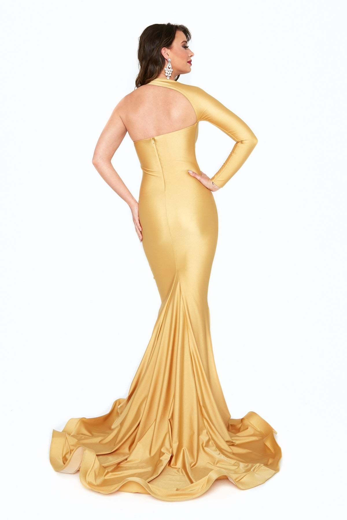 Woman wearing the Atria 6517H One-Sleeve Long Formal Dress—gold, fitted, with a mermaid skirt and long train—stands facing away from the camera against a white background.